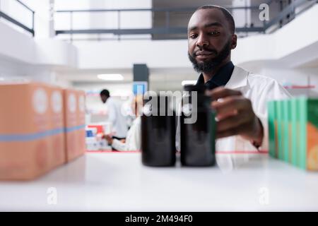 Pharmacien afro-américain prenant des bouteilles de supplément de l'étagère de pharmacie, l'accent sélectif sur l'homme. Pharmacie vendeur mettre des pilules gros plan, vendre des vitamines, pharmacie vue de face Banque D'Images