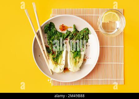 Assiette de délicieux chou pak choi à la sauce soya et verre d'eau sur fond jaune Banque D'Images