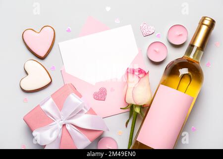 Lettre vierge avec rose, bouteille de vin, biscuits et cadeau sur fond gris. Célébration de la Saint-Valentin Banque D'Images