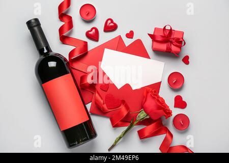 Lettre vierge avec rose, cadeau, cœur et bouteille de vin sur fond gris. Célébration de la Saint-Valentin Banque D'Images