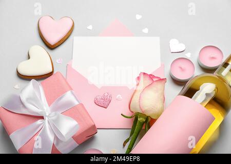 Lettre vierge avec rose, bouteille de vin, biscuits et cadeau sur fond gris. Célébration de la Saint-Valentin Banque D'Images