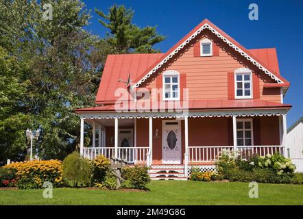 Ancienne maison de style cottage avec bordure de saumon et blanc datant de 1800s et cour avant paysagée en été. Banque D'Images