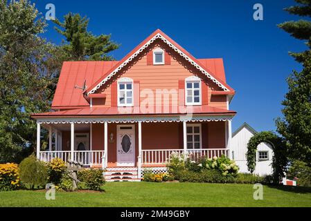 Ancienne maison de style cottage avec bordure de saumon et blanc datant de 1800s et cour avant paysagée en été. Banque D'Images