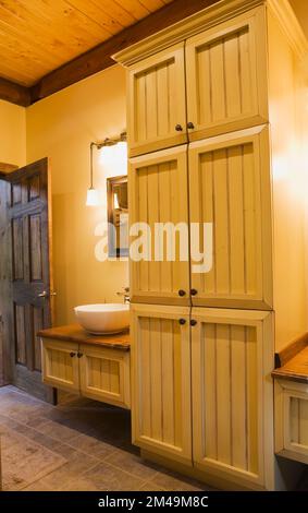 Lavabo blanc sur le comptoir de vanité en bois dans la salle de bains principale avec plancher de carreaux de céramique brun à l'intérieur de la maison en rondins. Banque D'Images