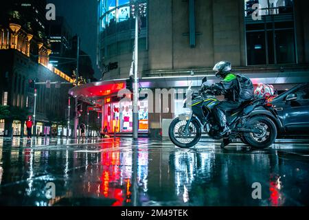 Un motocycliste s'arrête aux feux de signalisation lors d'une nuit de pluie avec des feux de circulation lumineux Banque D'Images