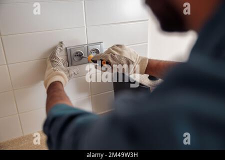 Gros plan d'un électricien professionnel avec un tournevis est en train de réparer la prise d'alimentation dans la cuisine Banque D'Images