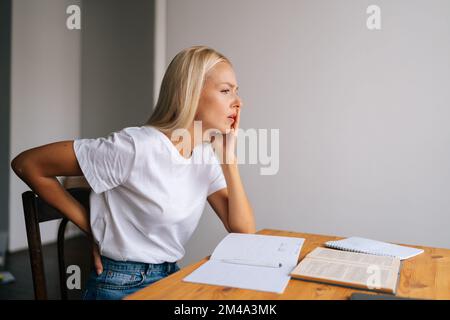 Vue latérale de la femme étudiant s'asseoir au bureau toucher arrière souffrent de spasme bas de la colonne vertébrale, mal malsain femme extensible ont un fort mal de dos. Banque D'Images