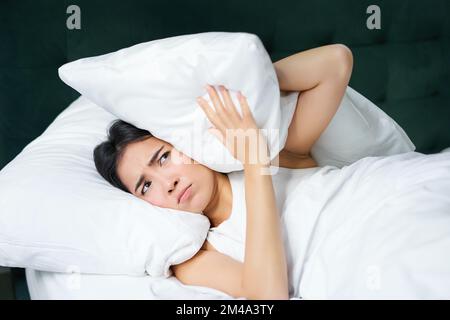 Insomnie. Asiatique fille ferme ses oreilles avec l'oreiller comme partenaire ronflant. Femme couché au lit, dérangé par le bruit la nuit, ne peut pas dormir Banque D'Images