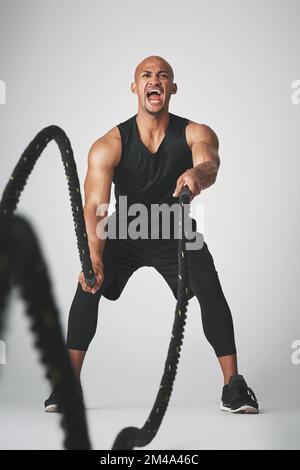 Lutte contre les cordes. Photo en studio d'un jeune homme sportif qui s'efforce avec des cordes de combat sur fond gris. Banque D'Images