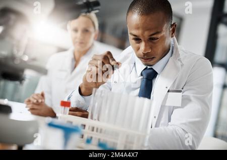 Tout au nom de la médecine. un beau jeune scientifique masculin teste un échantillon tout en faisant des recherches dans son laboratoire. Banque D'Images