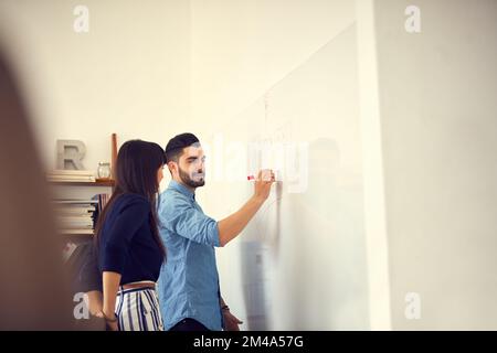 La productivité commence par un plan. un jeune homme d'affaires et une femme d'affaires ayant une séance de brainstorming sur un mur dans un bureau moderne. Banque D'Images