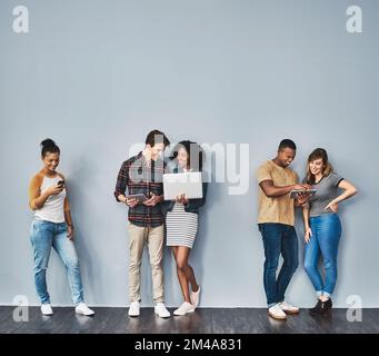 La génération technophiles. Photo en studio d'un groupe de jeunes utilisant la technologie sans fil sur fond gris. Banque D'Images