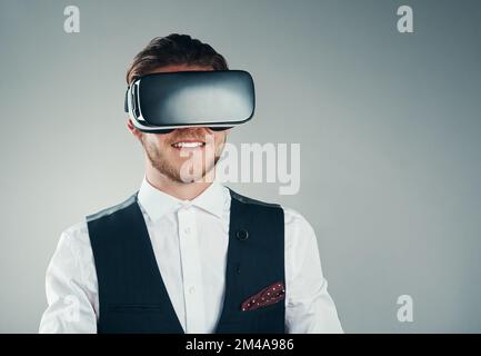 Faire des affaires dans le monde virtuel. Photo en studio d'un jeune homme d'affaires charmant utilisant un casque vr sur fond gris. Banque D'Images