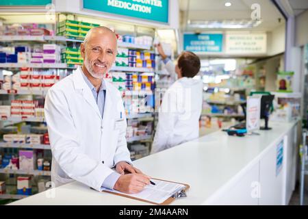 Nous devons nous assurer que nos stocks sont toujours pleins. Portrait d'un pharmacien mature écrivant sur un bloc-notes dans un chimiste. Banque D'Images