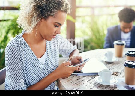 Shes a reçu un bloc-notes numérique pour stocker toutes ses idées. une jeune femme d'affaires utilisant un téléphone portable à l'extérieur avec ses collègues en arrière-plan. Banque D'Images