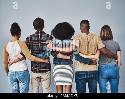 De bons amis se soutiennent mutuellement. Prise de vue en studio d'un groupe diversifié de jeunes s'embrassant les uns les autres sur un fond gris. Banque D'Images