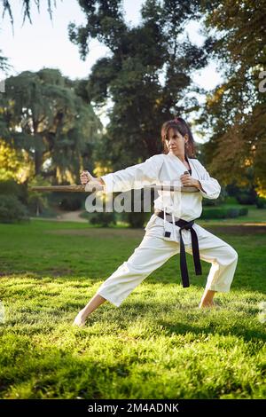 Femme carate combattant dans un kimono blanc et ceinture noire pratiquant le karaté à l'extérieur dans la nature. Sports et arts martiaux concept. Banque D'Images