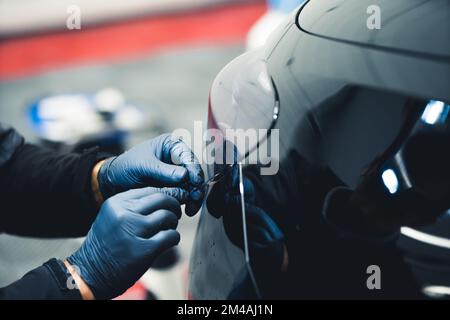 Gros plan d'une personne portant des gants bleus travaillant sur le feu arrière d'une voiture noire dans un garage. Détails de voiture. Prise de vue horizontale en intérieur . Photo de haute qualité Banque D'Images