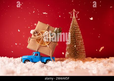 Une voiture-jouet porte un grand cadeau pour le nouvel an et Noël sur fond rouge Banque D'Images