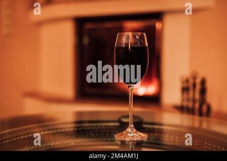 Un verre de vin rouge sur une table en verre près de la cheminée. Veille de Noël Banque D'Images