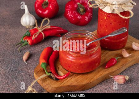 Sauce traditionnelle adjika au piment fort, collez l'harissa dans un pot en verre sur une table brune Banque D'Images