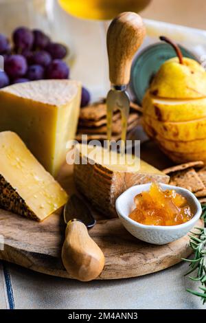 Différents types de fromage, fruits et confitures sur planche à découper en bois prêts pour la fête Banque D'Images