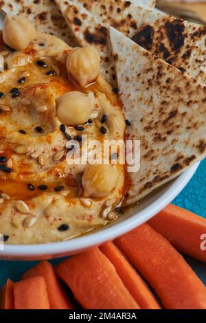 Du dessus, un bol de houmous délicieux avec des chips de tortilla placé près des tranches de carottes pendant le déjeuner Banque D'Images
