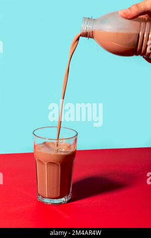 Personne méconnaissable versant du lait sucré au chocolat provenant d'une bouteille en plastique dans un verre sur fond de deux couleurs Banque D'Images