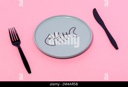 Du dessus de la plaque de céramique grise avec squelette de poisson peint servi sur la surface rose avec fourchette noire et couteau Banque D'Images