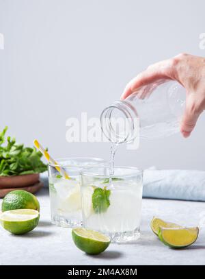 une main verse une limonade mojito lime dans un verre sur la table avec des tranches de lime et de la menthe fraîche. Vue avant et image d'espace de copie Banque D'Images