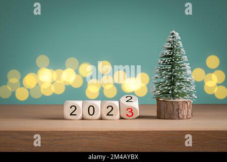 Mini arbre de Noël et blocs de bois avec le numéro d'année 2022 changeant à 2023 devant le fond vert. Concept de la nouvelle année. Banque D'Images