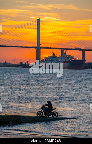 Le pont de Dartford traverse la Tamise au coucher du soleil avec un motard sur la jetée près de l'eau Banque D'Images