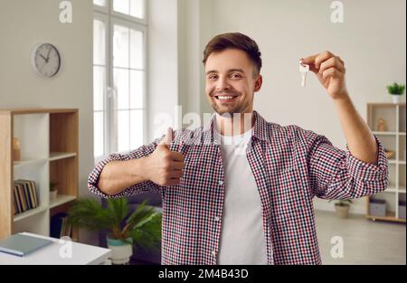 Homme heureux montrant les clés de sa nouvelle maison ou appartement, souriant et donnant des pouces vers le haut Banque D'Images