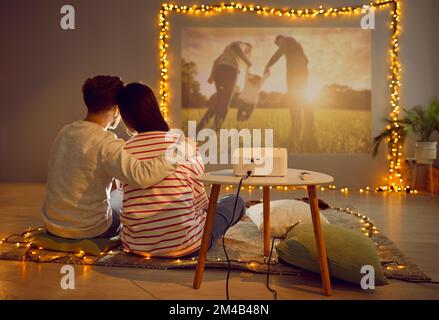 Couple amoureux heureux ayant un rendez-vous romantique à la maison, assis sur le sol et regardant le film sur le projecteur Banque D'Images