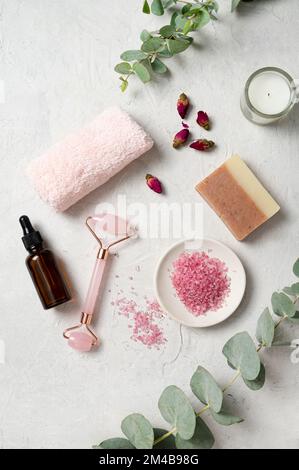 Sel de mer rose biologique avec rose, huile de massage, savon, serviette et bougie avec branche d'eucalyptus sur fond blanc texturé. Le concept de spa et nous Banque D'Images