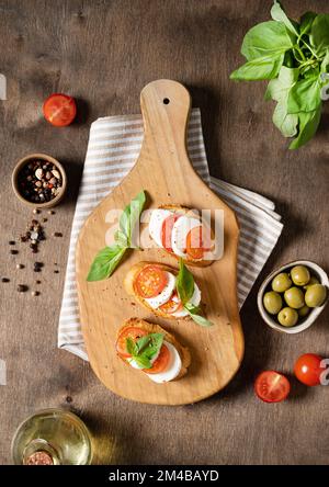 Sandwiches Caprese avec tomates fraîches, mozzarella et basilic frais et toast sur une planche à découper avec épices et huile d'olive sur un backgrou en bois Banque D'Images