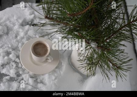 photo une tasse de café debout sur la neige et une branche d'un sapin dans un vase sur une table recouverte de neige Banque D'Images