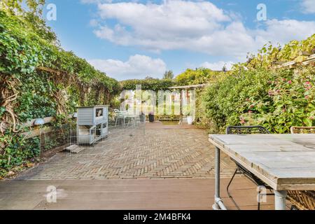 un patio extérieur avec des tables et des chaises au milieu, entouré de plantes vertes luxuriantes de chaque côté, il y a un ciel bleu Banque D'Images