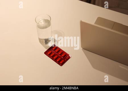 Le médicament avec une tasse d'eau sur la table blanche, le supplément nutritionnel autour de l'ordinateur portable Banque D'Images