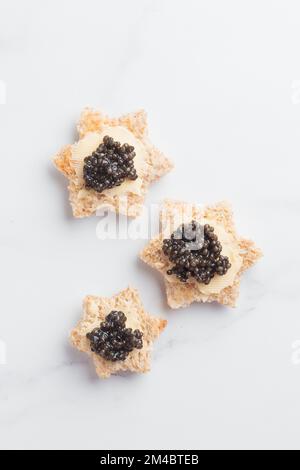 Caviar noir hors-d'œuvre étoiles de pain avec beurre sur fond blanc vue de dessus verticale Banque D'Images