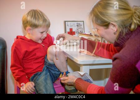 Pays-Bas, Arnhem; mère met de l'iode sur le genou blessé de son fils qui pleure. Banque D'Images