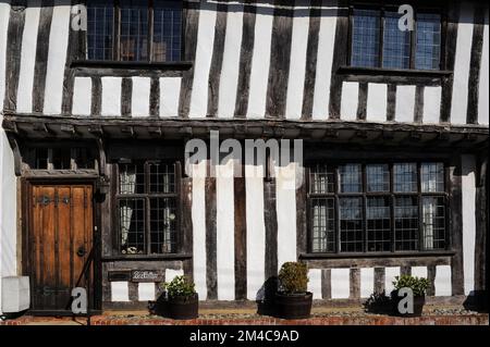 Penchée à droite : étage supérieur à colombages et à l'embarcadère de Box Cottage dans Prentice Street, Lavenham, Suffolk, Angleterre, Royaume-Uni. La maison, construite en 1400s ou 1500s, se dresse sur un haut plinthe de briques et a des fenêtres en chêne à meneaux, des lumières au plomb, des poutres apparentes et des solives et une fenêtre en tableau arrière à trois lumières sur sa porte d'entrée. Banque D'Images