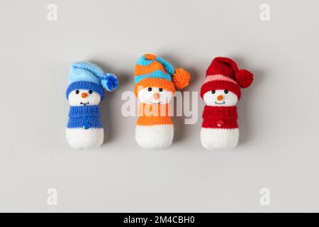 Trois bonhommes de neige tricotés amusants en chapeaux et chandails rouge, bleu et orange sur fond gris. Carte de vœux de Noël et du nouvel an 2023 Banque D'Images