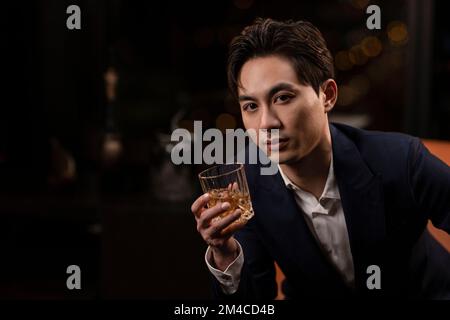 Élégant homme chinois qui boit du whisky Banque D'Images