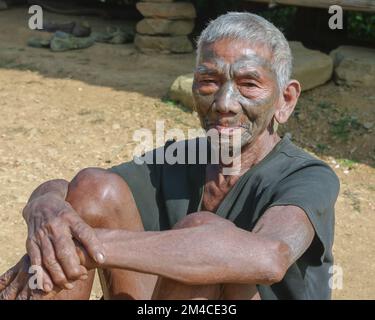 Quartier mon, Nagaland, Inde - 11 20 2010 : Portrait de l'ancien chasseur de tête de tribu Naga Konyak guerrier avec tatouage traditionnel visage assis à l'extérieur Banque D'Images