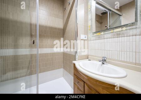 Salle de bains avec petit lavabo en porcelaine blanche sur comptoir en marbre blanc et miroir en marbre de verre avec armoires en chêne et cabine de douche à parois de verre Banque D'Images