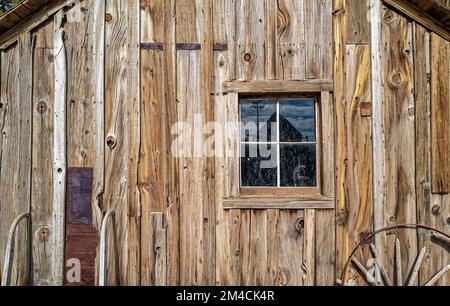 L'ancienne roue de wagon repose sous la fenêtre d'un mur rustique de cabine Banque D'Images