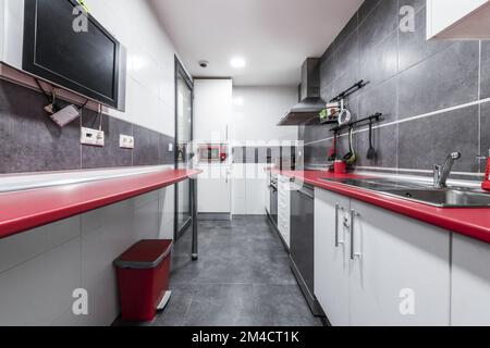 Cuisine traditionnelle d'une maison urbaine avec des meubles en bois rouge et blanc avec appareils assortis, sols en grès et carreaux sur les murs et les sols gris Banque D'Images