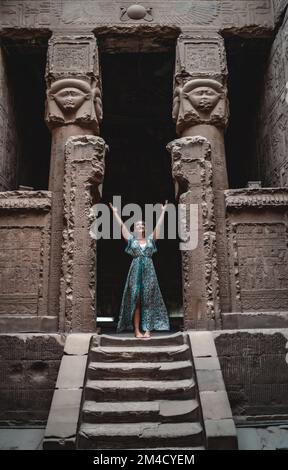 Une belle femme de race blanche pieds nus vêtue d'une robe bleue explorant le Temple de Hathor. Dendera, Égypte. Banque D'Images