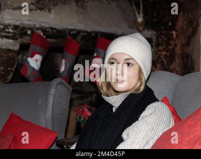 Une fille en vêtements de laine est assise dans un fauteuil avec des oreillers rouges sur le fond de la décoration de Noël Banque D'Images